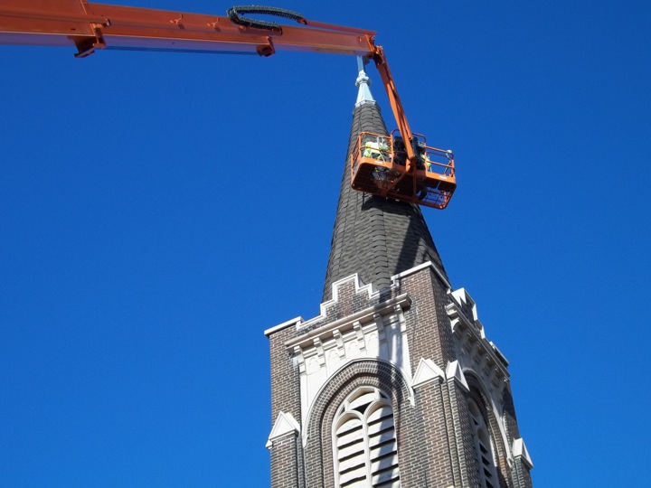 Roofing being replaced on a spire using a boom lift