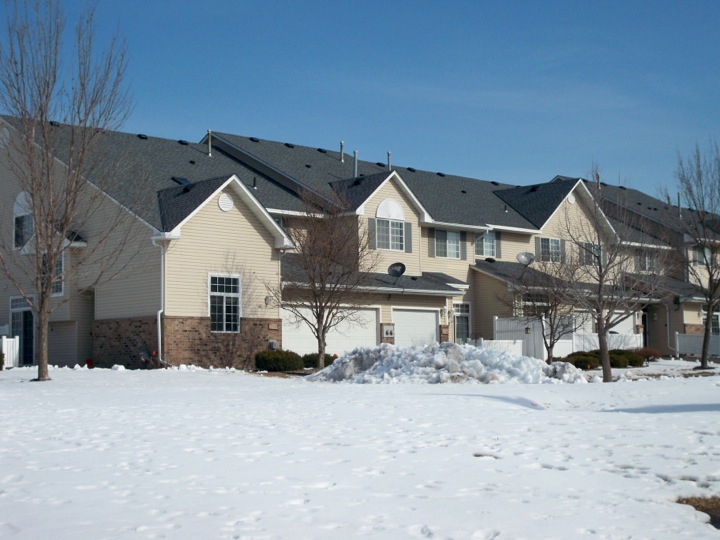 A row of yellow townhomes viewed from across a field of snow