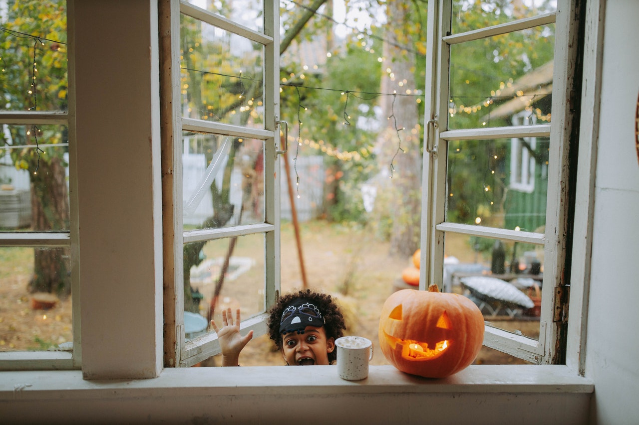 Young boy looking into window next to pumpkin and Halloween decorations.