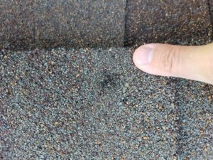Finger pointing to a damaged area on a roof shingle