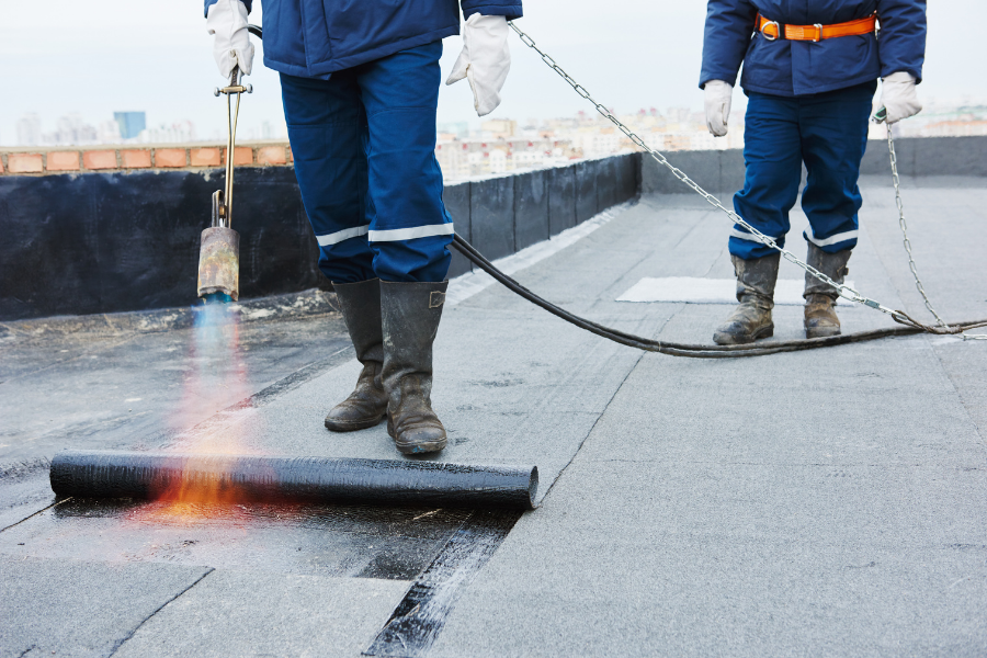 Two roofing contractors using fire to apply PVC roofing membrane on commercial roof.