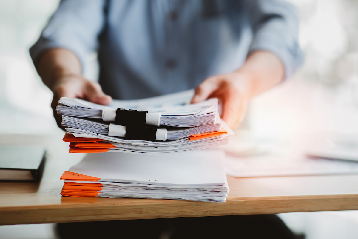 Insurance claims paperwork stack held out by person wearing a blue button-down shirt.