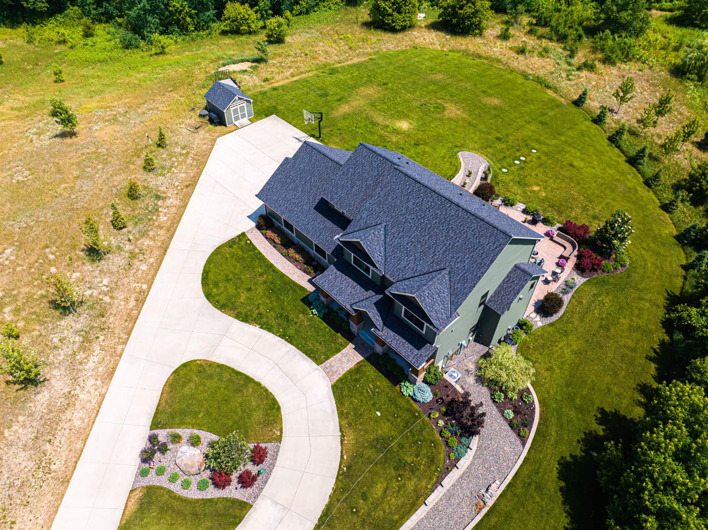 Aerial view of a home that features dark asphalt roofing and a wraparound driveway